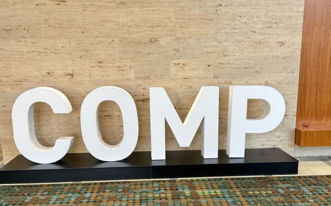 Large white COMP letters on a stand at the National Comp 2025 conference