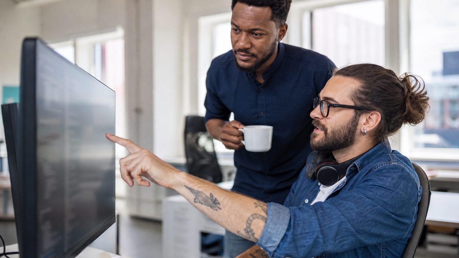 Two developers reviewing code together at a monitor in a bright office